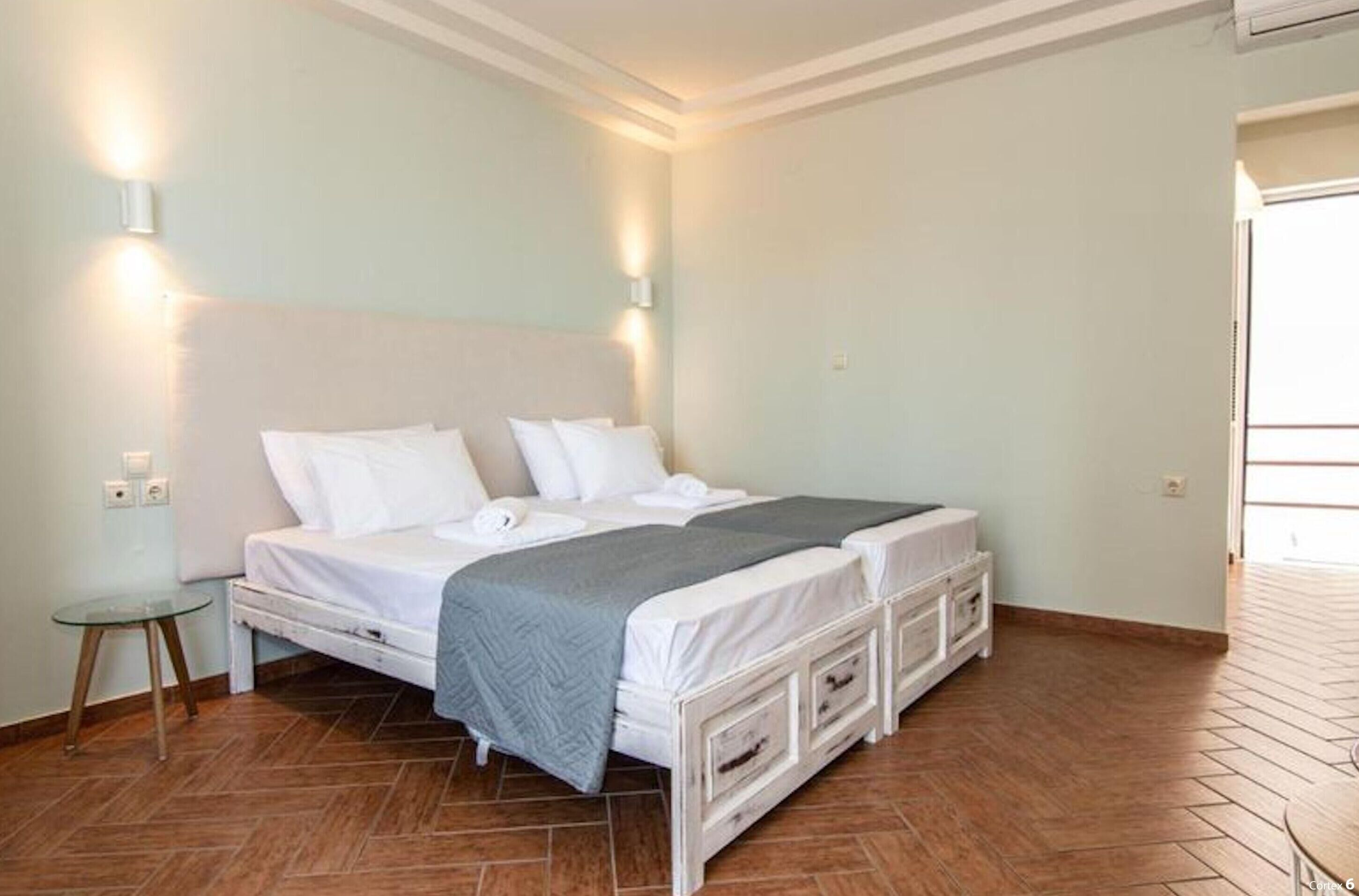 Una cama doble con una manta gris, dos mesitas de noche y una lámpara de pared.