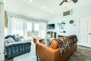 A living room with a sofa, a coffee table, and a TV. There is a door and a window with curtains. - Cape Allswell - Life is Good, Sun, Sand & Surf! (Freeport)