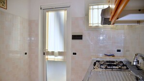 A kitchen with a gas stove, a sink, and a window with a curtain. - Quiet Retreat in Bibione Pineda (San Michele al Tagliamento)
