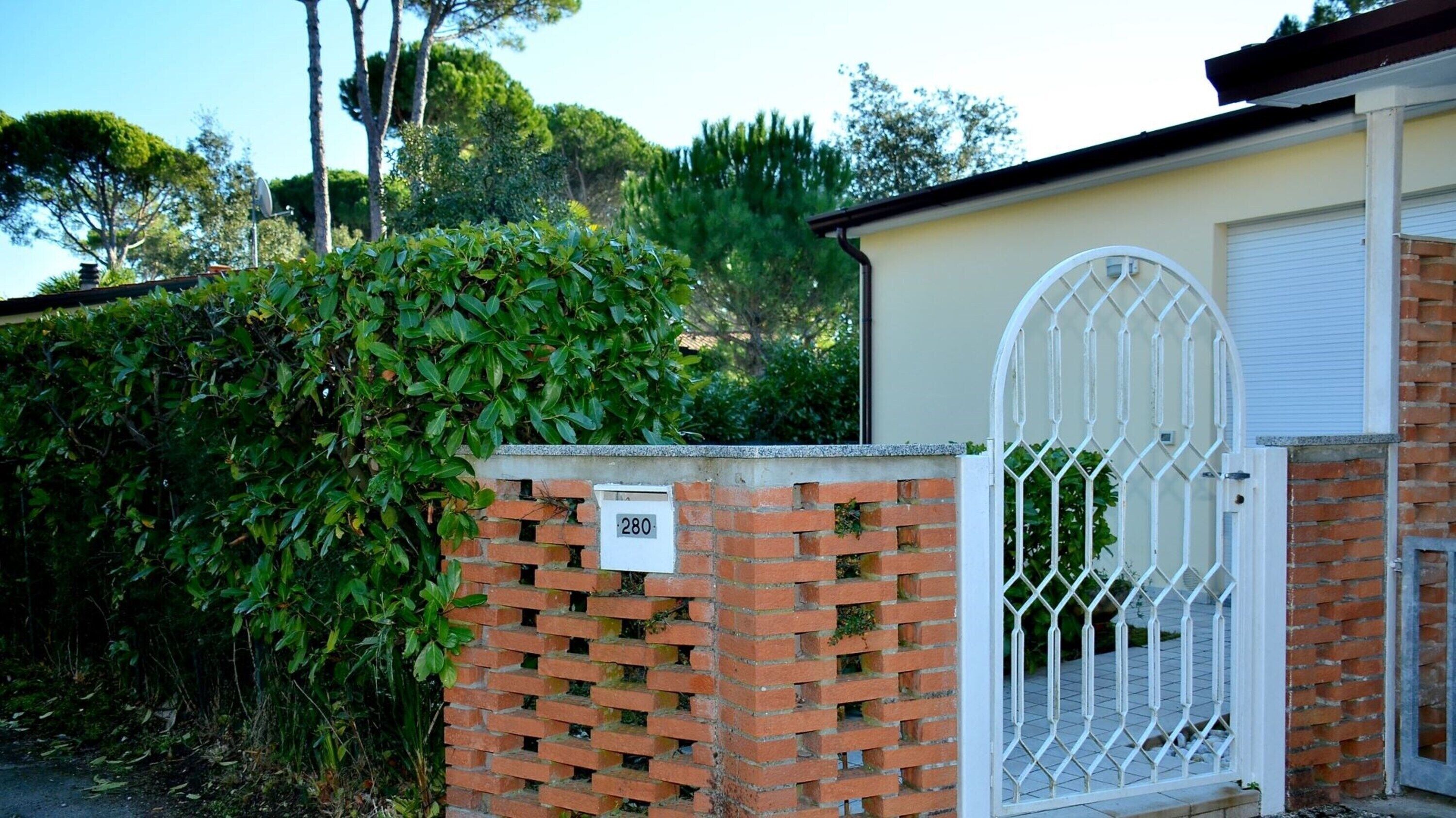 Une entrée fermée par un portail, avec un mur en briques et un portail en métal, une boîte aux lettres portant le numéro 280, et un bâtiment doté d’une porte de garage.