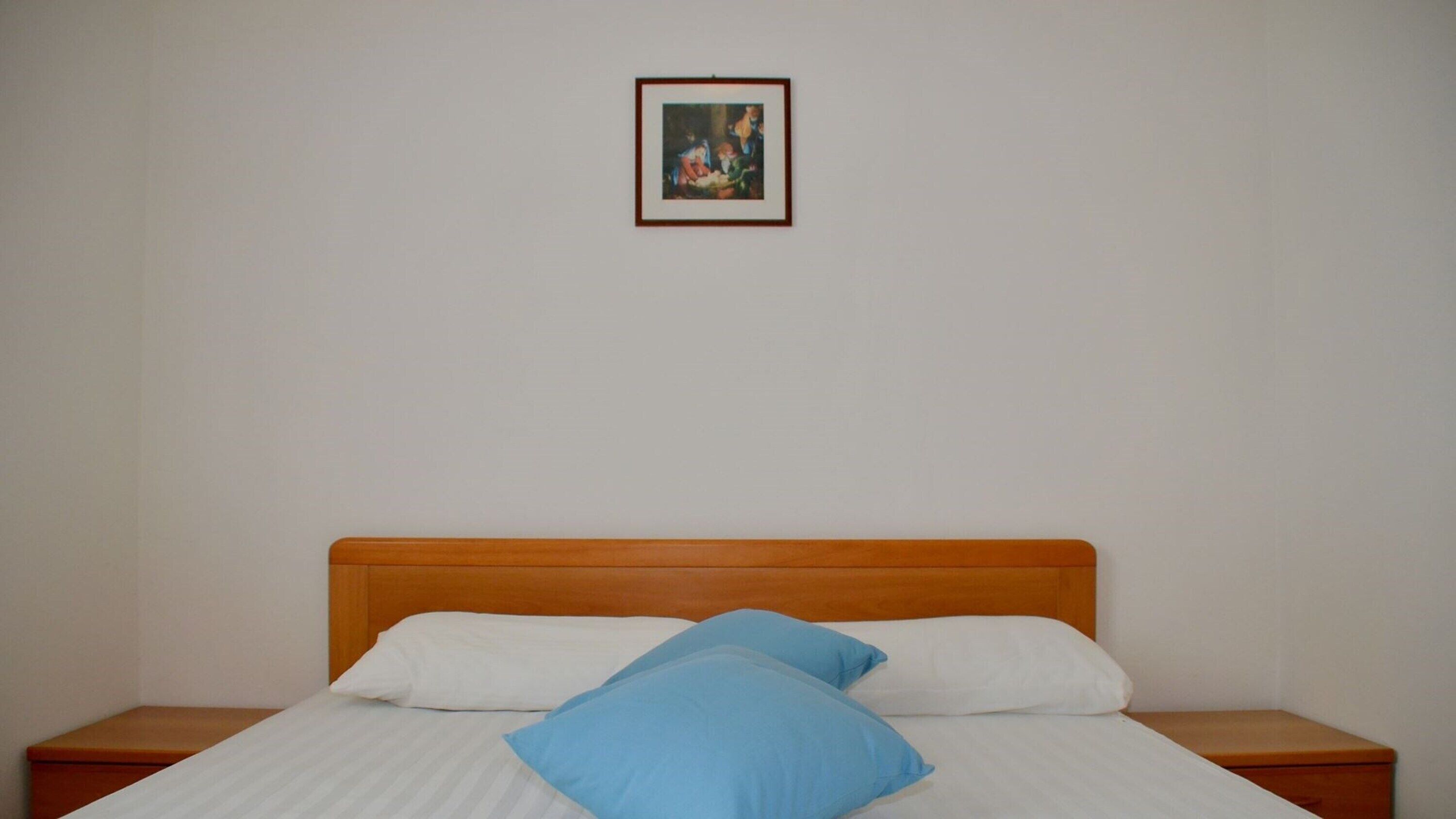 A single bed with white and blue pillows, a wooden headboard, and a framed picture on the wall.