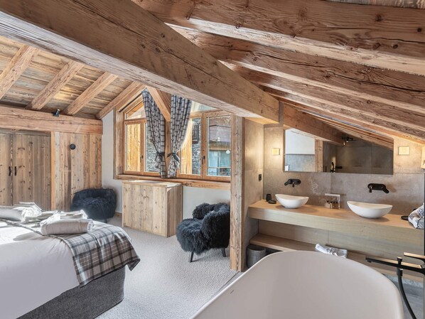 Ein rustikales Schlafzimmer aus Holz mit einem großen Bett, einem kleinen Stuhl, einer Badewanne und einem Fenster mit Vorhängen.