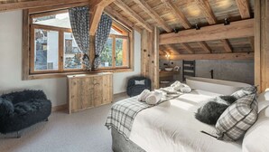A cozy bedroom with a wooden ceiling, a large window with curtains, a bed with pillows, and a small wooden table. - Renovated chalet with pool, sauna and hammam for 14 people in Saint-Martin-de-Belleville (Saint-Martin-de-Belleville)