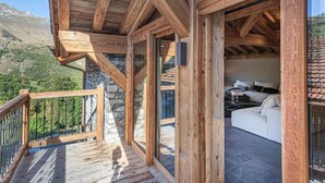 A wooden balcony with a stone wall, a white sofa, and a view of the mountains. - Renovated chalet with pool, sauna and hammam for 14 people in Saint-Martin-de-Belleville (Saint-Martin-de-Belleville)