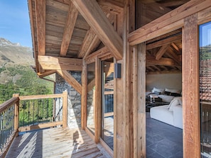 Un balcone in legno con pareti in pietra, un divano bianco e vista sulle montagne.