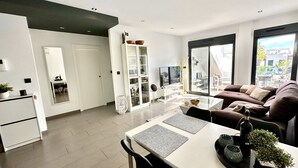 A modern living room with a sofa, a dining table, and a kitchen area with cabinets and a refrigerator.