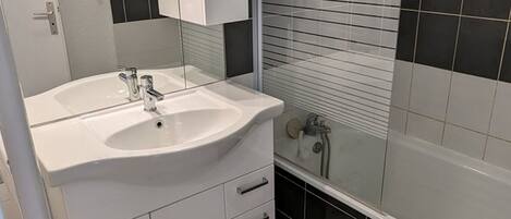 Un baño con un lavamanos blanco, dos espejos, una bañera y paredes con azulejos blanco y negro.