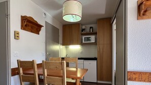 A compact kitchen with wooden cabinets, a microwave, and a dining table with chairs. - Apartment 5 ppl, 6th floor, WIFI, ski locker, La Plagne (Plagne Soleil)