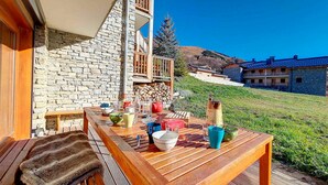 Eine Holzterrasse mit Esstisch, Steinmauern und freiem Blick auf eine Hügelkuppe mit Gebäuden.