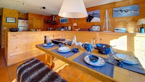 Ein Interieur einer Holzhütte mit Essbereich, gedeckt für eine Mahlzeit, inklusive Tisch mit blau-weißen Tellern, einer Pendelleuchte und Holzwänden.