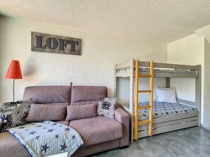 Una habitación con una cama individual superpuesta, un sofá con cojines estampados, una lámpara de pie roja y un letrero en la pared que dice "LOFT".