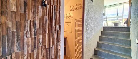 Eine Holzwand mit Struktur, eine Treppe mit Geländer und eine Tür mit Kleiderhaken.