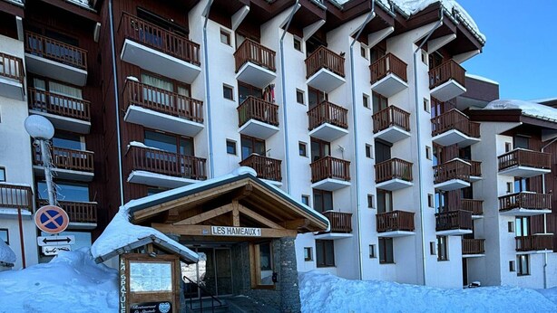 Ein mehrstöckiges Hotel mit Balkonen, einem Schild mit der Aufschrift "LES HAMEAUX 1" und einem kleinen Eingangsbau mit einem Schild für "La Spatule".