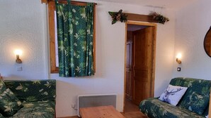 Ein gemütliches Zimmer mit einem Holztisch, zwei grün gepolsterten Sofas, einem Fenster mit Vorhängen und Wandleuchten.