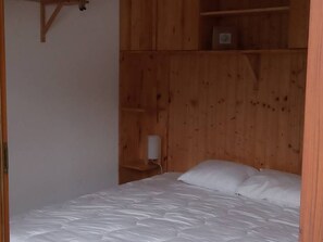 A bedroom with a wooden wardrobe, a bed with white bedding, and a nightstand with a lamp. - Spacious 3-room apartment, ski-in/ski-out with parking, St Jean d'Aulps (Saint-Jean-d'Aulps)