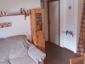 A room with a bed, a wooden cabinet with glass doors, a shelf with books and figurines, and a door leading to another room. - Spacious 3-room apartment, ski-in/ski-out with parking, St Jean d'Aulps (Saint-Jean-d'Aulps)