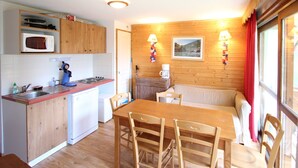 Una cocina compacta con armarios de madera, un microondas y una estufa. Hay una zona de comedor con una mesa y sillas de madera, y un sofá.