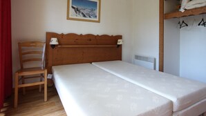 Un dormitorio con una cama de madera, una silla, un estante en la pared con ropa y un cuadro enmarcado.