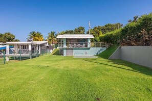 A small, single-story building with a flat roof, a covered patio area, and a grassy lawn.