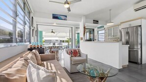 A modern kitchen with a central island, a dining area with a glass table, and a living room with a sofa and chairs. - Pao de Azucar | Surf Haven with Spectacular Views (Rincón)