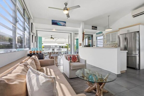 A modern kitchen with a central island, a dining area with a glass table, and a living room with a sofa and chairs.