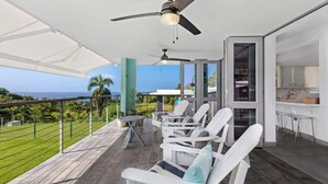 A covered outdoor seating area with white chairs and a ceiling fan, overlooking a scenic view. - Pao de Azucar | Surf Haven with Spectacular Views (Rincón)