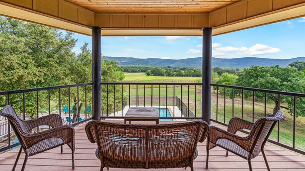 A covered outdoor area with wicker furniture, a pool, and a view of a green landscape. - NO bunk beds | Golf course & hill country views, private swimming pool, huge outdoor kitchen (Concan)