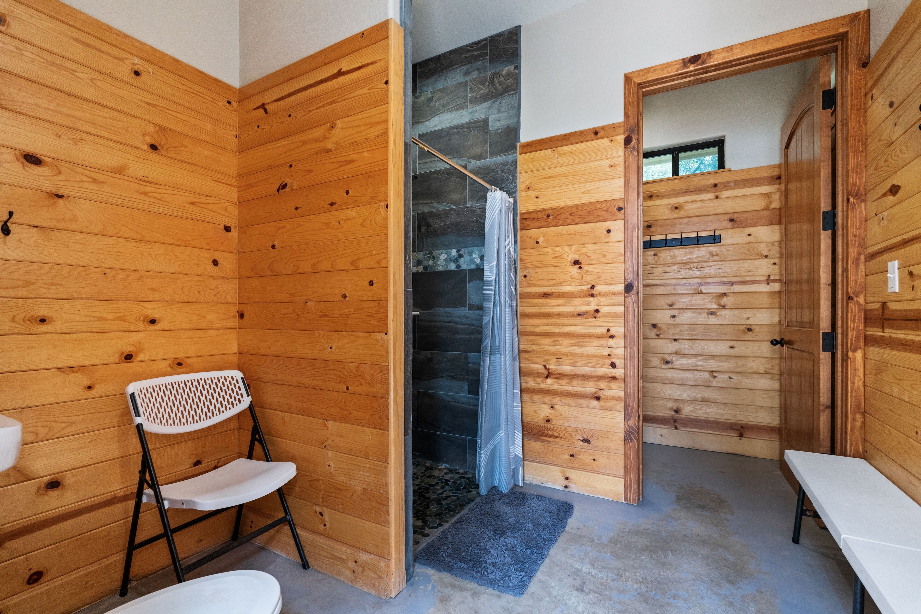 Una habitación con paneles de madera, una ducha, un banco y una pequeña mesa.