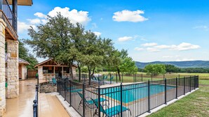 A swimming pool with a black fence, surrounded by a grassy area and trees. - NO bunk beds | Golf course & hill country views, private swimming pool, huge outdoor kitchen (Concan)