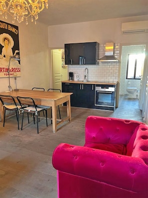 A modern kitchen with black cabinets, a white tiled backsplash, and a stainless steel sink. There is a dining area with a wooden table and chairs, and a bright red sofa in the foreground. - 15. Charming 1-bedroom apartment in the Old Town of Villefranche (Villefranche-sur-Mer)