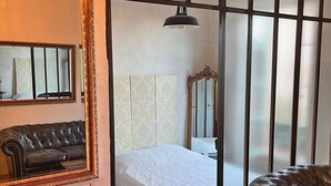 Et hotelværelse med en stor skydedør, en seng med hvidt sengetøj, en rød lænestol, en sort lædersofa og et spejl med gylden ramme.