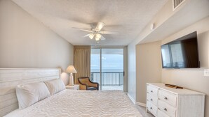A hotel room with a bed, a dresser, a TV, a chair, and a balcony with a view. - Ashworth 1605 | Oceanfront Four Bedroom Condo (North Myrtle Beach)