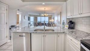 A kitchen with white cabinets, a granite countertop, and a dishwasher. - Ashworth 1605 | Oceanfront Four Bedroom Condo (North Myrtle Beach)
