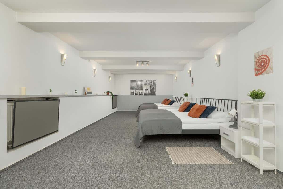 A modern hotel room with a kitchenette, two beds, a white wardrobe, and a small seating area.