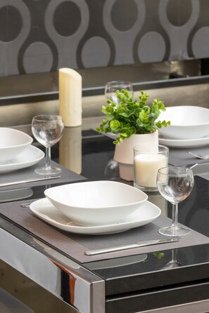 A modern kitchen with a black countertop, white plates, a glass of water, a candle, and a small potted plant. - Spacious Apartment with Terrace | Close to Wawel Castle, Place to Work (Kraków)