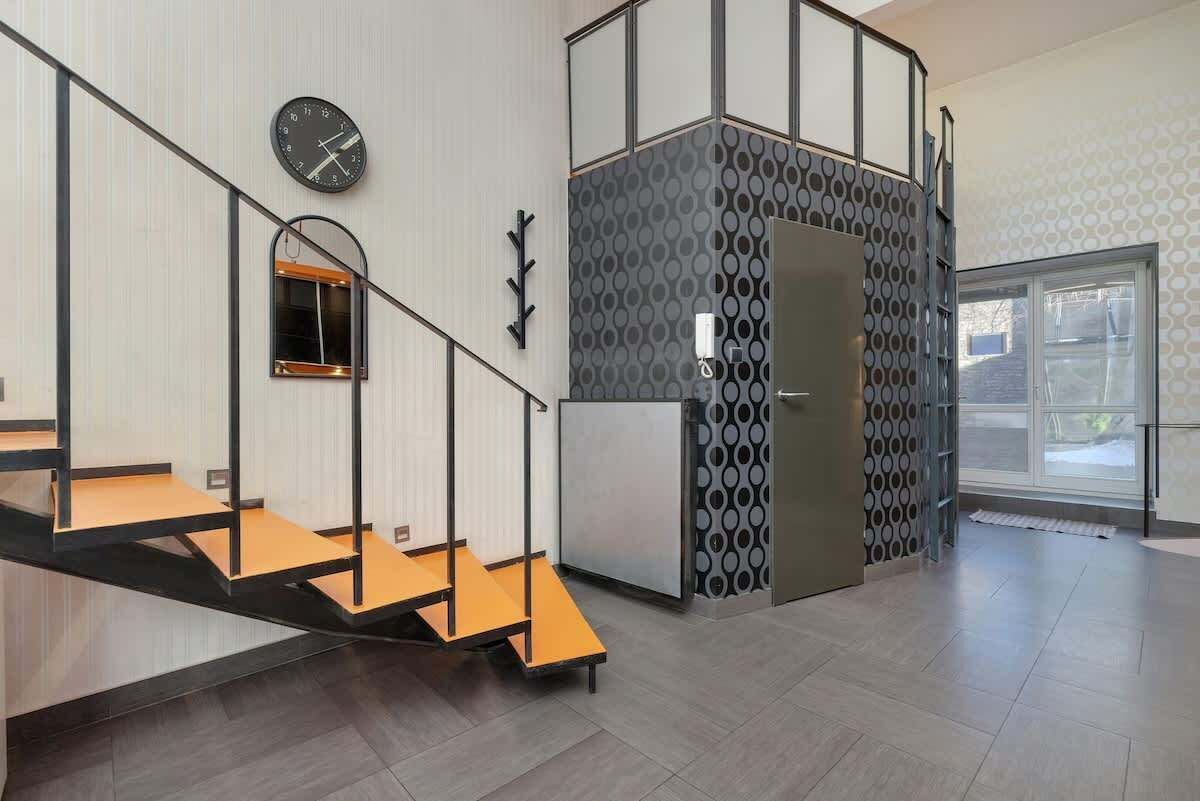 A modern interior with a staircase, a clock, and a patterned wall.