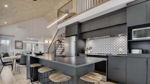 A modern kitchen with a central island, bar stools, and a staircase leading to an upper level.