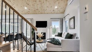 A modern living room with a staircase, a fireplace, a sofa, and a television.