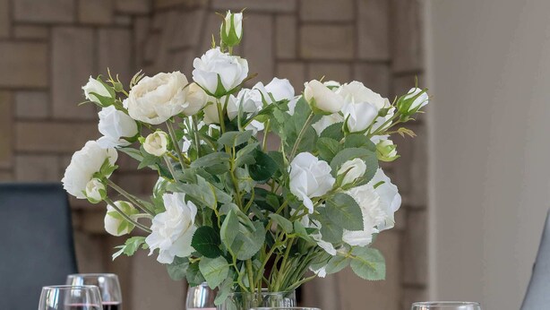 Une table décorée avec des roses blanches dans un vase, entourée de verres à vin.