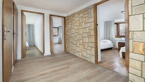 Un couloir doté d’un plancher en bois, de panneaux muraux en pierre, et une chambre avec un lit et une fenêtre.