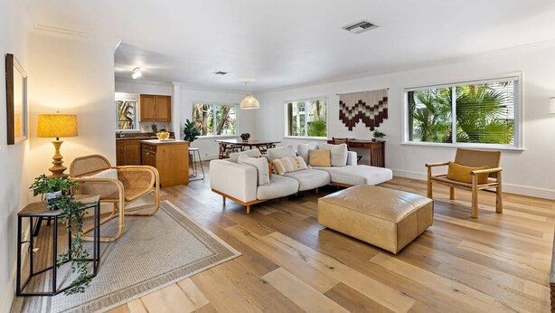 A spacious living area with a large sofa, a coffee table, and a dining table. There is a kitchen area in the background with wooden cabinets and a dining table. - Bohemian Condo Near Las Olas and Beach (Fort Lauderdale)