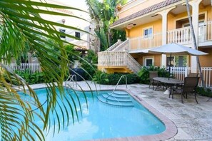 A pool area with a staircase leading to a balcony, surrounded by greenery and a building with a tiled roof. - Bohemian Condo Near Las Olas and Beach (Fort Lauderdale)