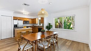 A modern kitchen with wooden cabinets, a stainless steel refrigerator, and a dining area with a wooden table and chairs. - Bohemian Condo Near Las Olas and Beach (Fort Lauderdale)