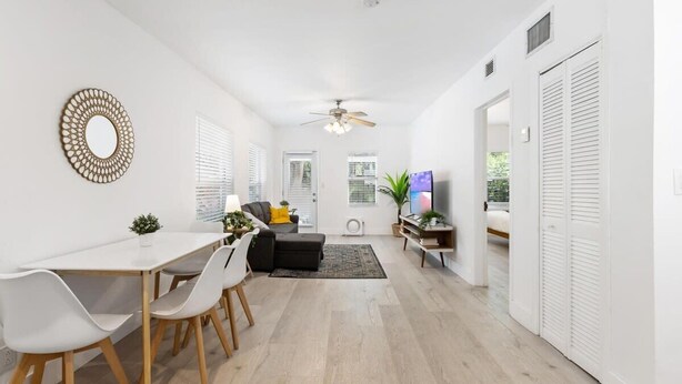 A modern living room with a dining area, white walls, and a ceiling fan. - Near Beach and Las Olas, 1 bedroom Apartment (Fort Lauderdale)