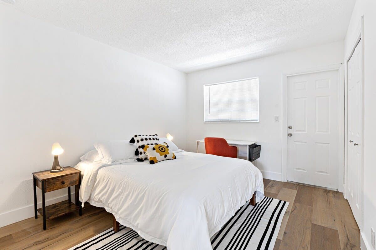 A bedroom with a bed, bedside table, lamp, and a chair.