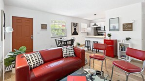 A modern living room with a red leather sofa, a glass coffee table, and a dining area with a red cabinet and bar stools. - Chic Sailboat Bend Condo w/Parking, Near Riverwalk (Fort Lauderdale)