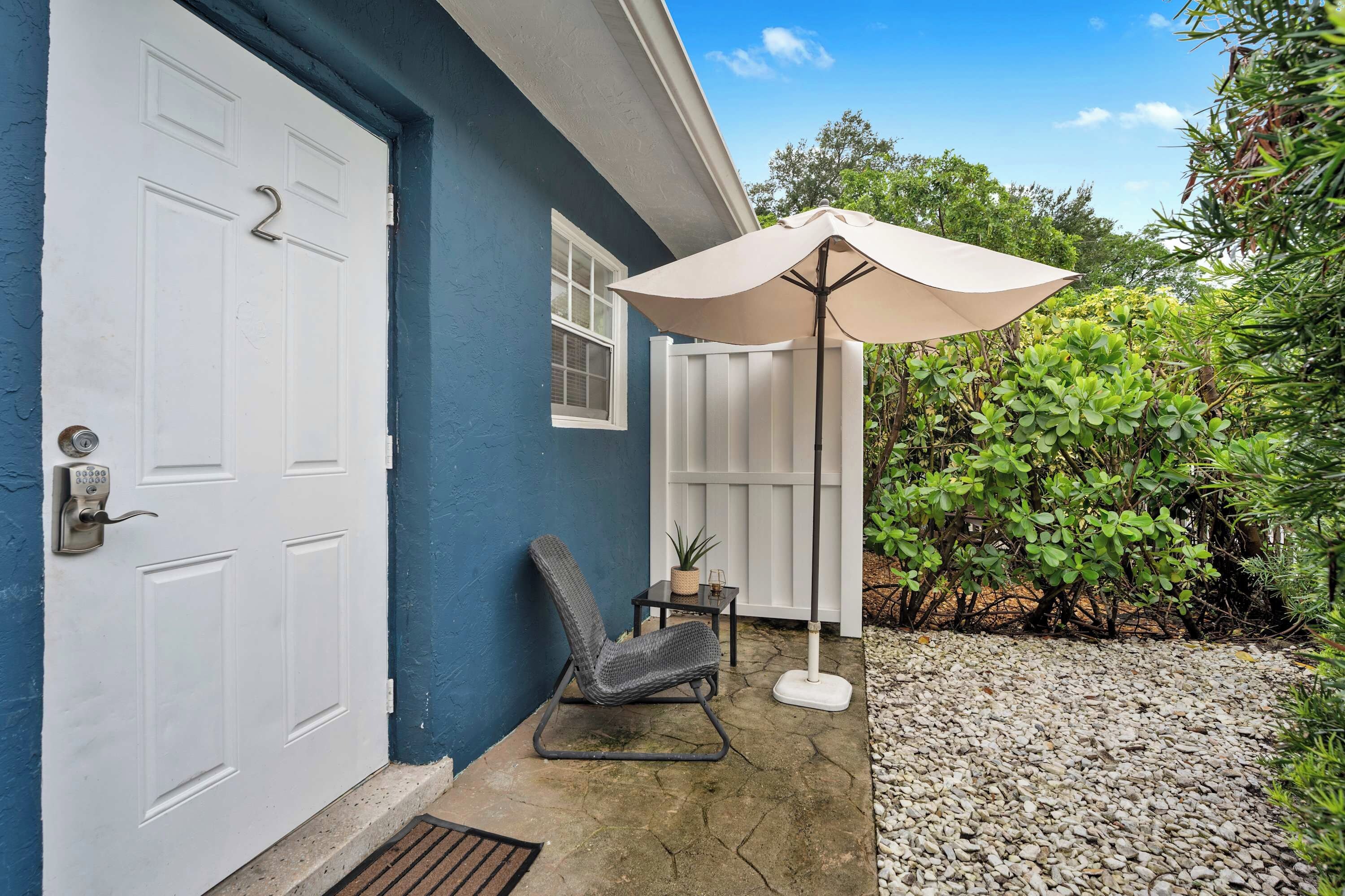 A house with a blue exterior, a white door, and a patio area with a chair and an umbrella.