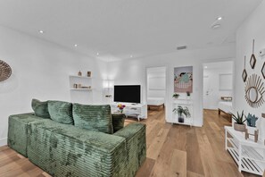 A modern living room with a green sofa, a flat-screen TV, and a white coffee table. - Chic Condo w/ Patio, Near Fort Lauderdale Hotspots (Fort Lauderdale)