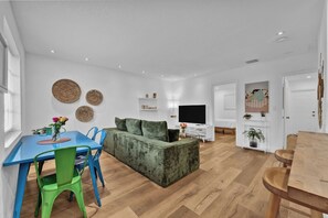 Un salon moderne avec un canapé, un téléviseur et un coin repas avec des chaises.