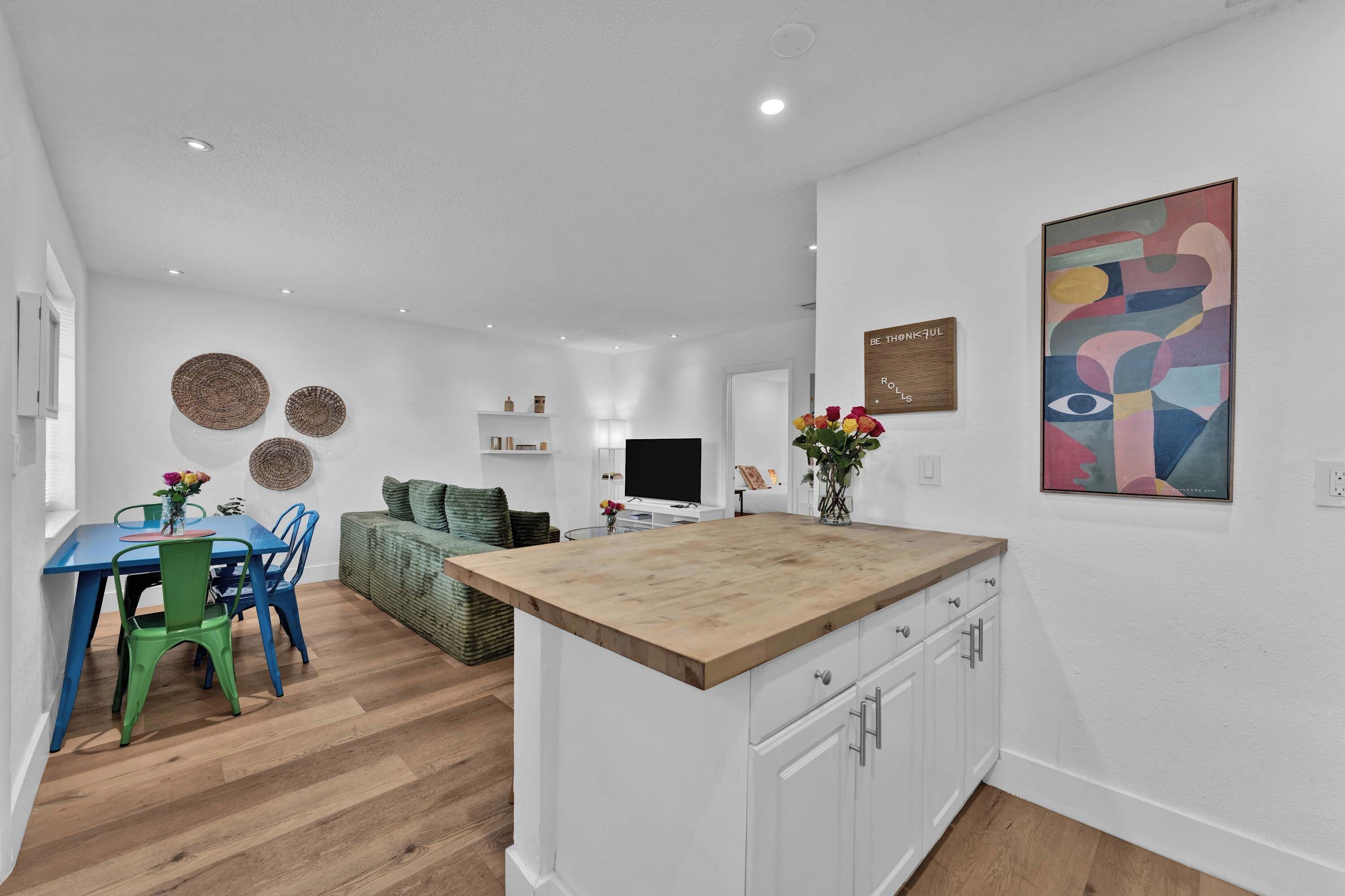 A modern kitchen with a wooden island, white cabinetry, and a dining area with blue chairs.